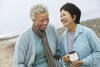 two older women laugh as they walk on the beach